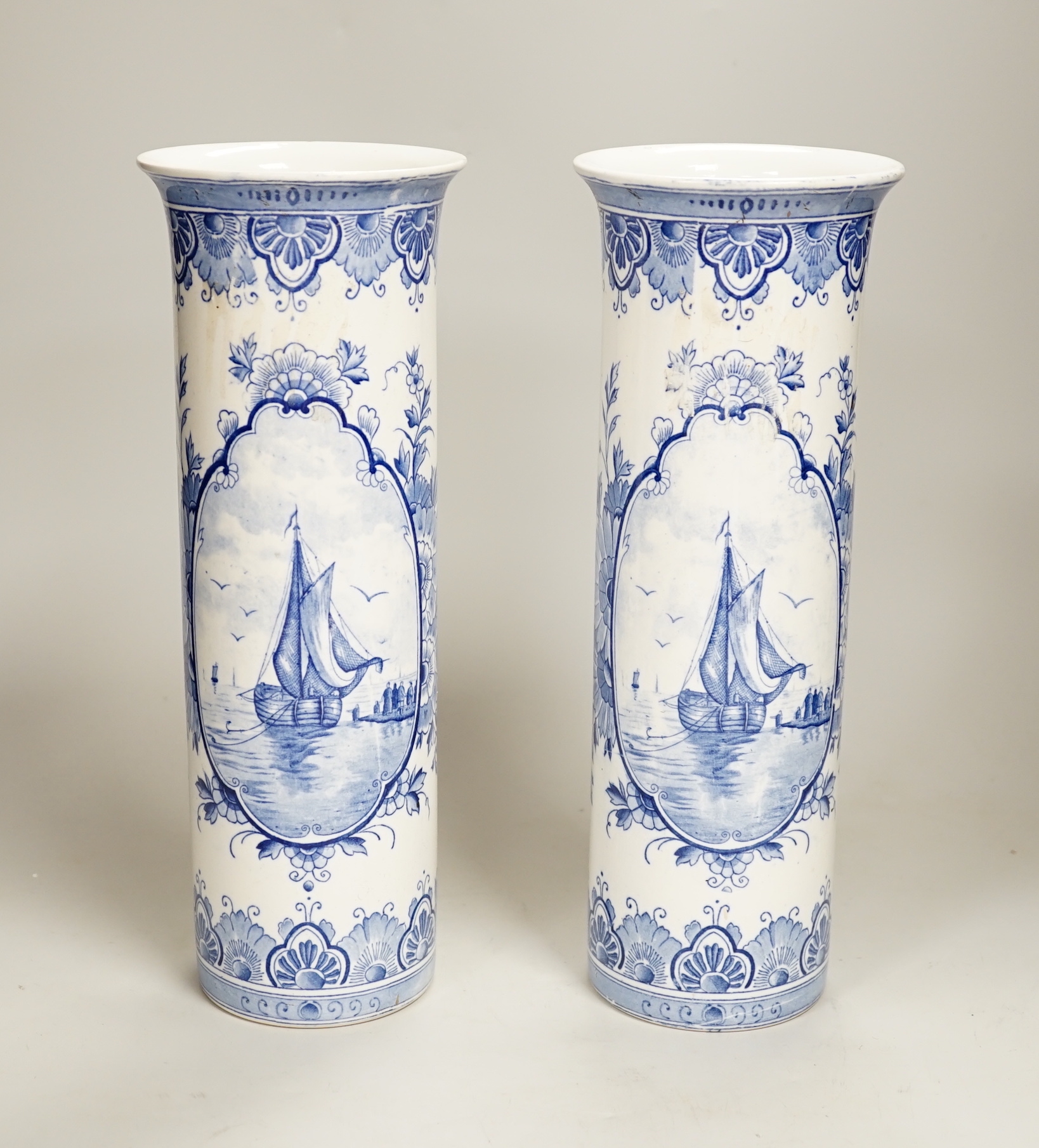 A pair of Delft blue and white cylindrical vases, each decorated with boats, 30cm high